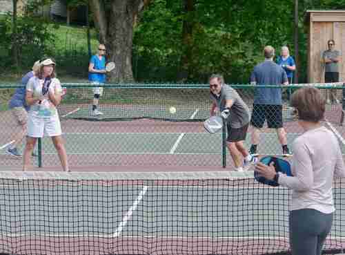 A group of players enjoying a game on outdoor pickleball courts Belfast. Players are engaged in a doubles match, focusing on volleys at the net. The scene showcases a lively atmosphere with players of different ages participating.