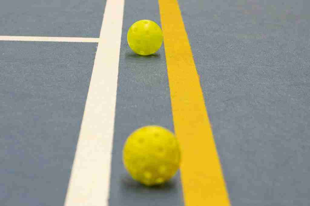 Two yellow pickleball balls positioned near a white and yellow line on an indoor court, illustrating the line rule in pickleball.
