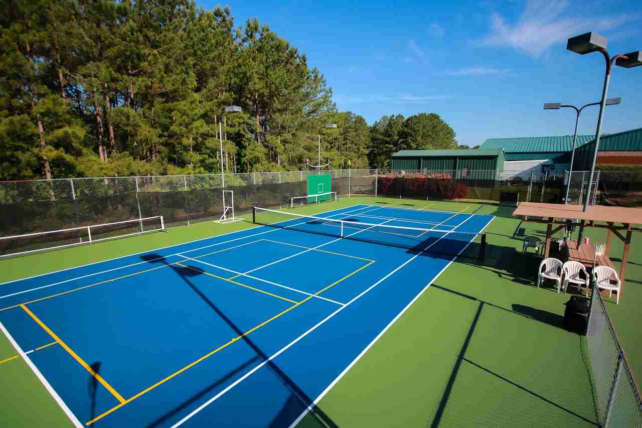 A tennis court converted for pickleball with blue and green surface markings, featuring two pickleball nets and surrounding greenery, demonstrating how you can play pickleball on a tennis court.