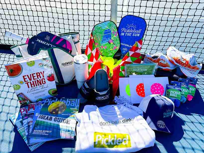 A collection of pickleball gifts, including paddles, balls, magazines, apparel, and accessories, displayed on a court, perfect for pickleball enthusiasts.