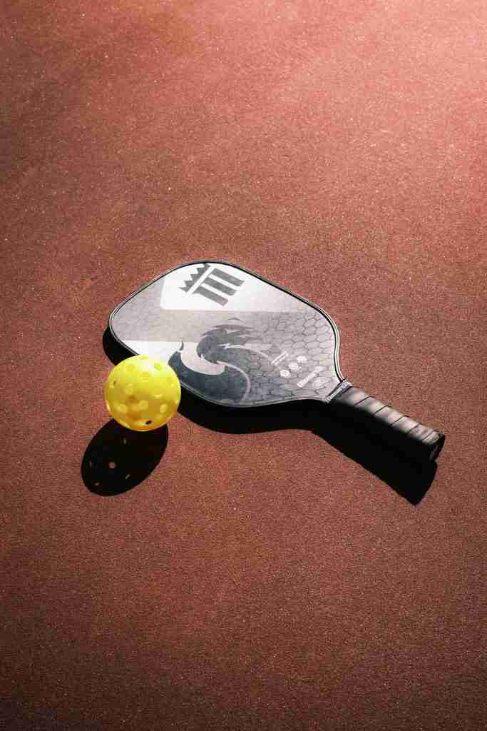 A pickleball paddle and a bright yellow pickleball resting on a red court, perfect items to consider as gifts for pickleball players.