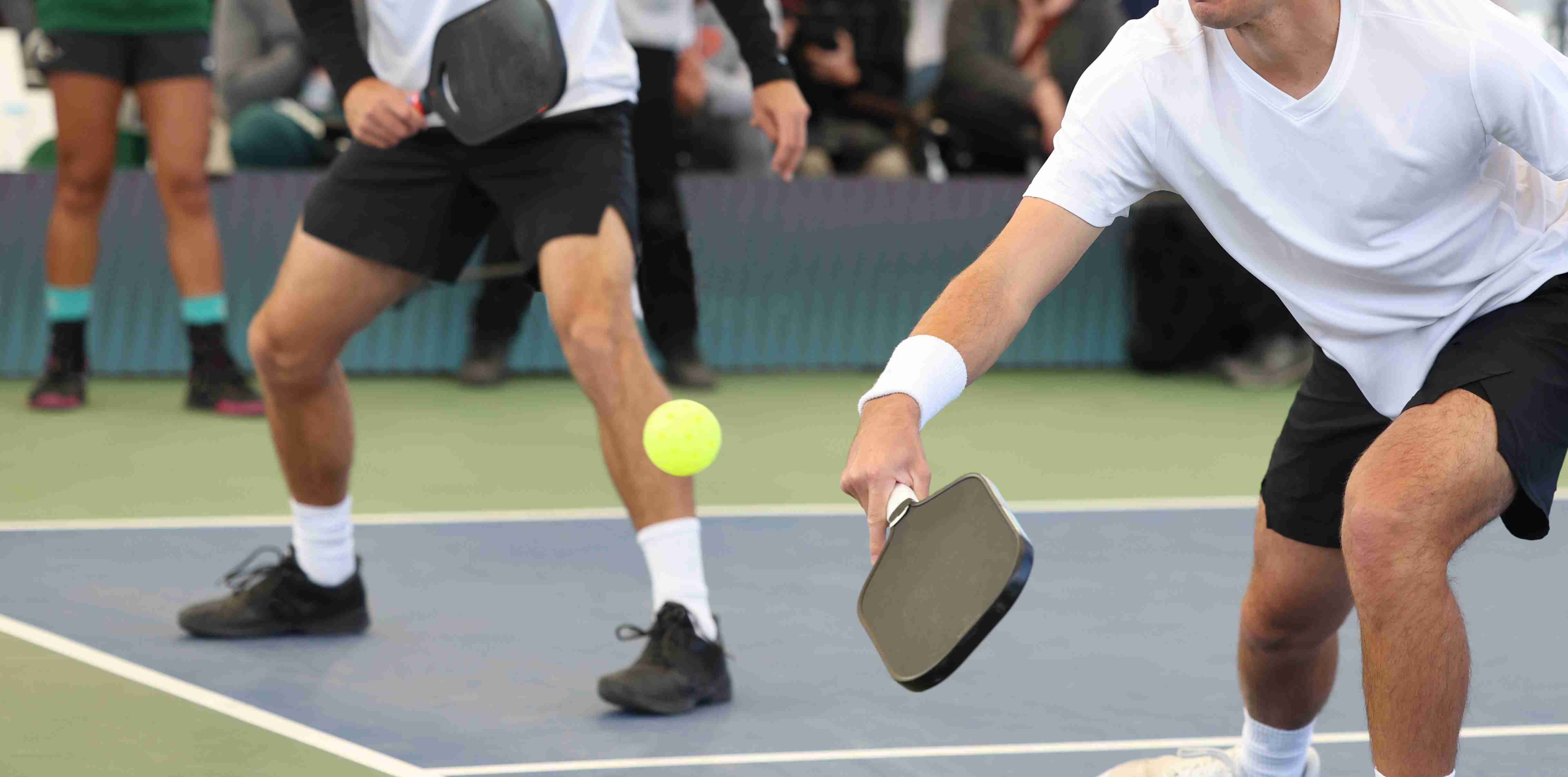 two people playing pickleball on a court with black paddles