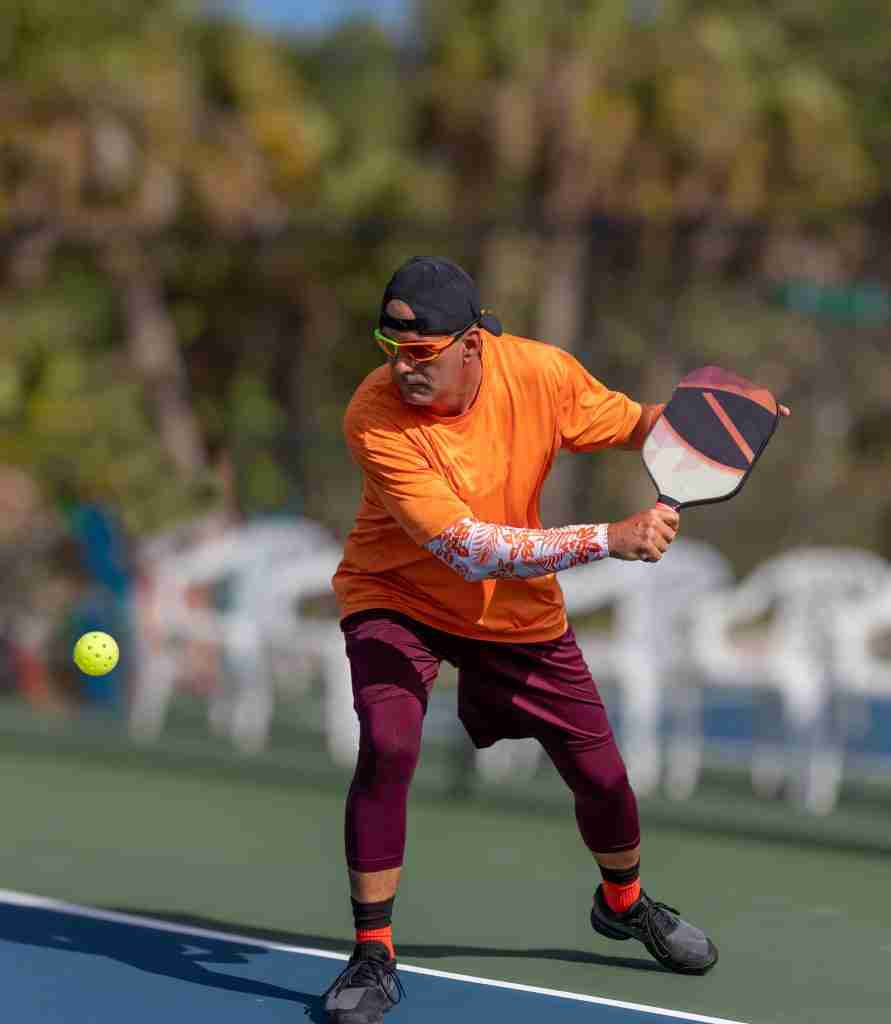 A male pickleball player in bright athletic gear prepares to hit a shot with one of the best pickleball paddles 2025 on an outdoor court.