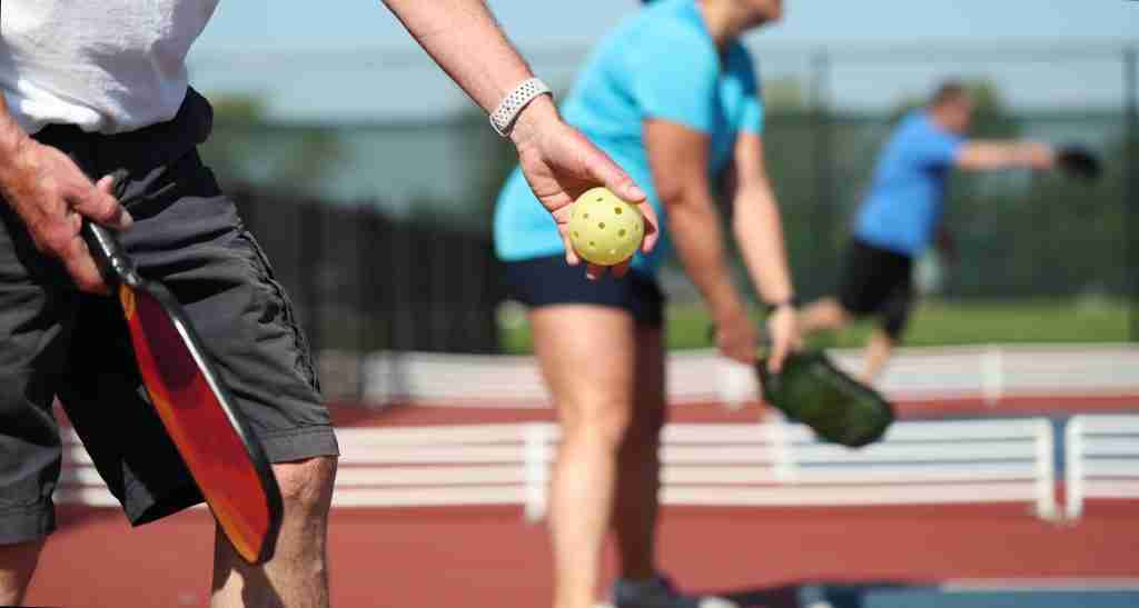 Players preparing to serve on an outdoor court, demonstrating pickleball serve rules with paddle and ball in hand.