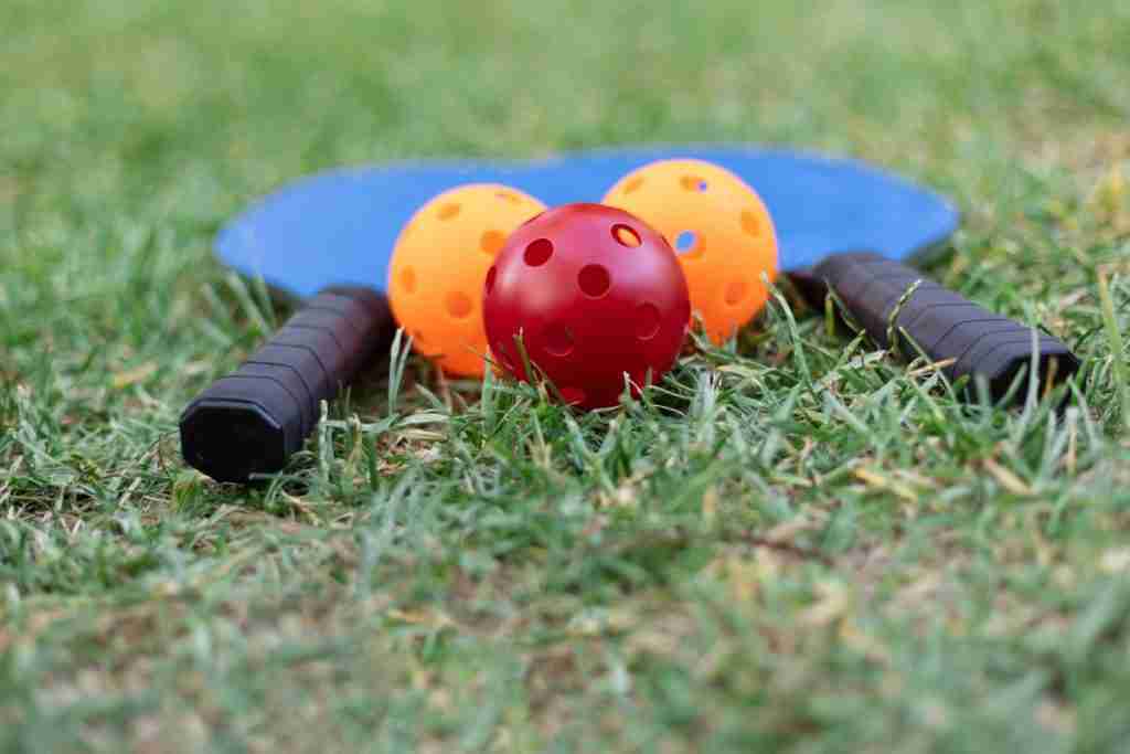 Can you play pickleball on grass with two paddles and colorful balls lying on a lawn.