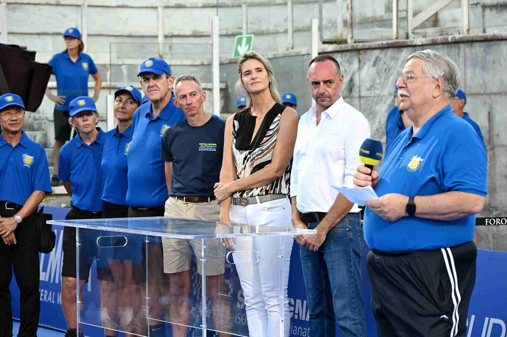 Officials and event organizers stand together during the opening ceremony of the European Pickleball Championships 2025 in Rome, with one speaker addressing the audience.