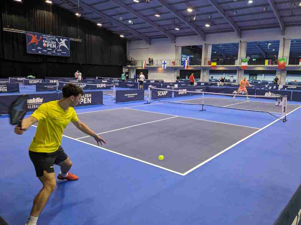 Indoor pickleball tournament action on a blue court, illustrating the high standard clubs can achieve when learning How to Start a Pickleball Club.
